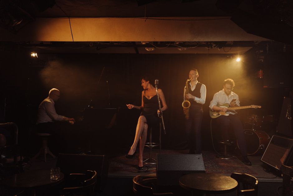 A jazz band performing with a female singer and musicians playing piano, saxophone, and guitar on stage.